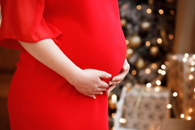 Una ragazza incinta con una camicia bianca da uomo abbraccia il suo bambino dentro Sullo sfondo c'è un albero di Natale