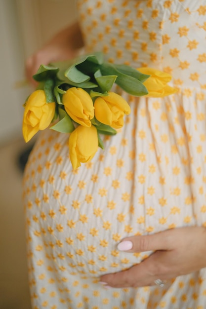 Una ragazza incinta tiene tulipani gialli vicino all'addome
