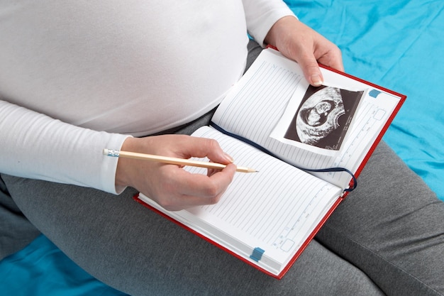 Una ragazza incinta tiene un quaderno e una foto di un'ecografia Record e preparazione per la nascita del bambino