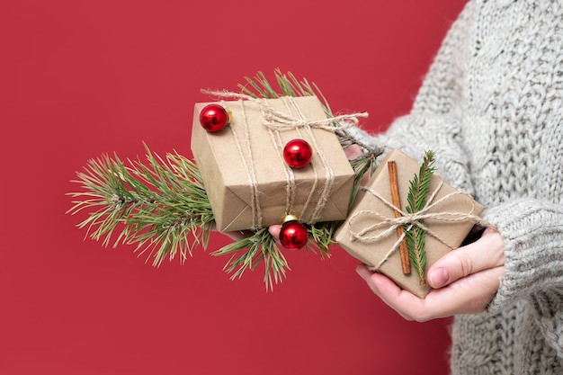 Una ragazza irriconoscibile con un maglione tiene i regali di Natale su uno sfondo rosso. Scatole regalo fatte a mano nelle mani di una donna. Sfondo di Capodanno con bellissimi regali.