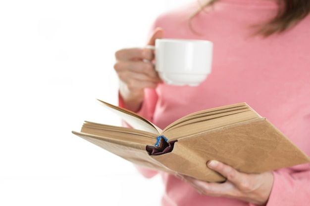 Una ragazza legge un libro e tiene in mano una tazza di caffè.