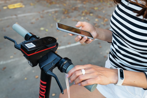 Una ragazza noleggia uno scooter elettrico con un'applicazione sul suo telefono. Noleggio self-service di scooter elettrici su strada.