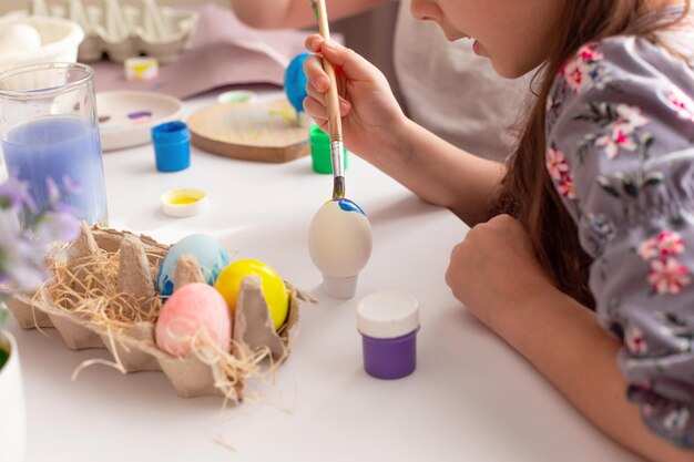 Una ragazza seduta a un tavolo bianco dipinge le uova
