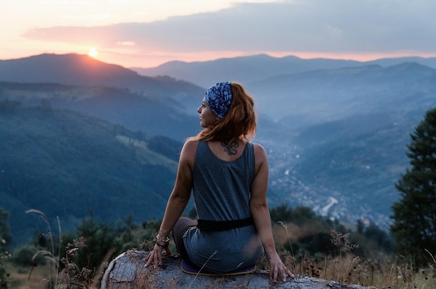 Una ragazza si siede sul bordo della scogliera e guarda la valle del sole e le montagne Donna seduta sulla cima della montagna e contempla il tramonto Tramonto nei Carpazi ucraini
