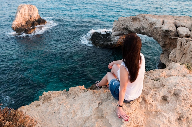 Una ragazza si siede sul bordo di una scogliera e guarda il mare