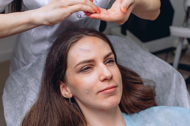 Una ragazza si sottopone a una procedura in un salone termale da un abile cosmetologo che le applica una crema sul viso.