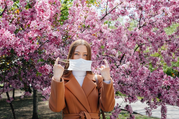 Una ragazza si toglie la maschera e respira profondamente dopo la fine della pandemia in una giornata di sole primaverile, di fronte a giardini fioriti. Protezione e prevenzione covid 19.