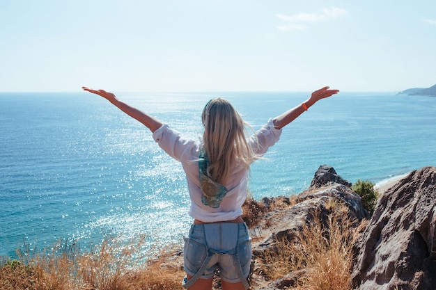 Una ragazza si trova su una montagna con una camicia bianca vicino al mare