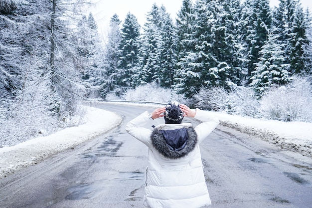 Una ragazza si trova su una strada deserta intorno a alberi ad alto fusto, close-up. Persone su una strada d'inverno. Sogni di viaggio. Viaggio invernale