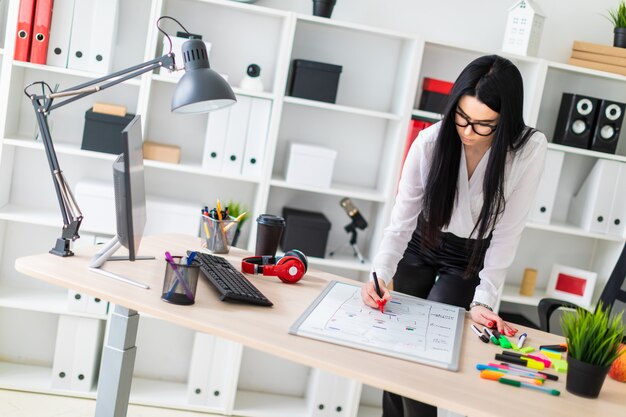 Una ragazza si trova vicino a una scrivania del computer e disegna un pennarello su una lavagna magnetica.