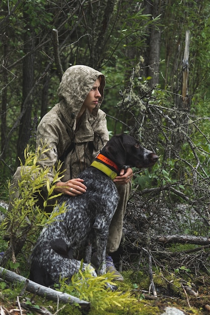 Una ragazza siede nel bosco con il suo cane da caccia. Una ragazza in un comuffle caccia un'anatra con il suo drathaar tedesco