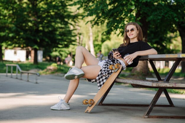 Una ragazza skater adolescente si sta rilassando sulla panchina con uno skateboard nel parco degli skater