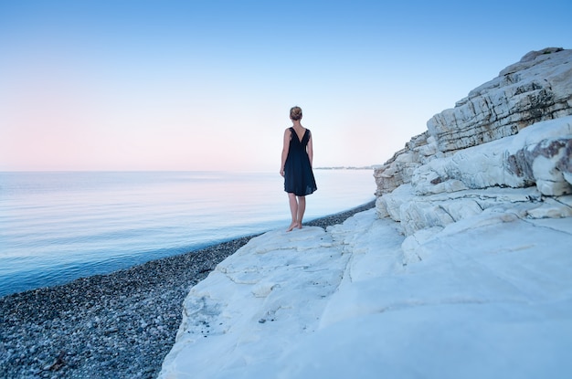 Una ragazza solitaria in abito nero si trova in riva al mare. Rocce bianche Il concetto di minimalismo.