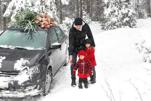 Una ragazza sorride dolcemente in piedi accanto a suo padre, sorella e un'auto con un albero di Natale e regali