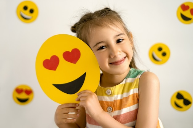 una ragazza sorridente con tutti i denti tiene tra le mani un'emoji d'amore