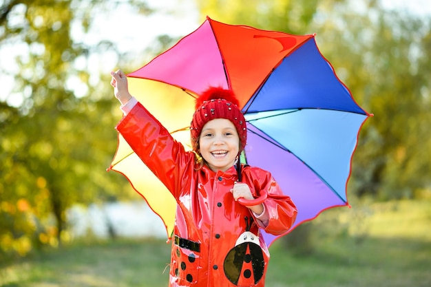 Una ragazza sorridente con un cappello rosso e una giacca rossa cammina con un ombrello arcobaleno in natura