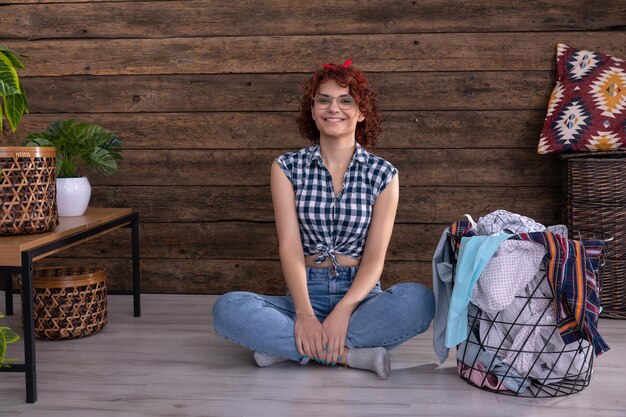 Una ragazza sorridente con una camicia a quadri si siede sul pavimento accanto al bucato