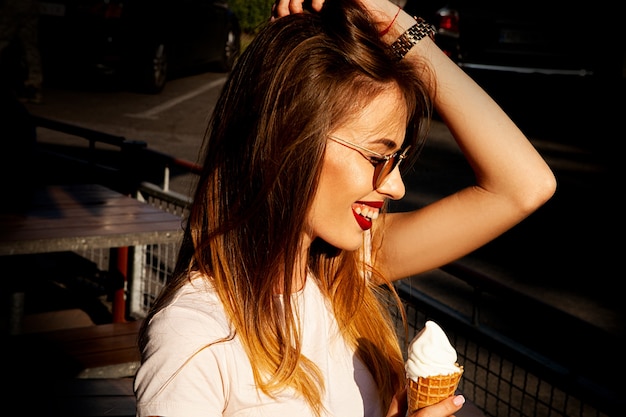 Una ragazza sotto i raggi del sole al tramonto sta mangiando un gelato in città.