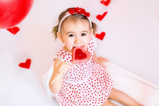 Una ragazza sta mangiando una caramella a forma di cuore. Un bambino in abito bianco con cuori celebra un giorno di innamorati