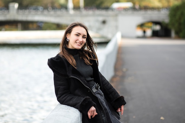 Una ragazza sta sull'argine vicino all'acqua, in abiti pesanti.