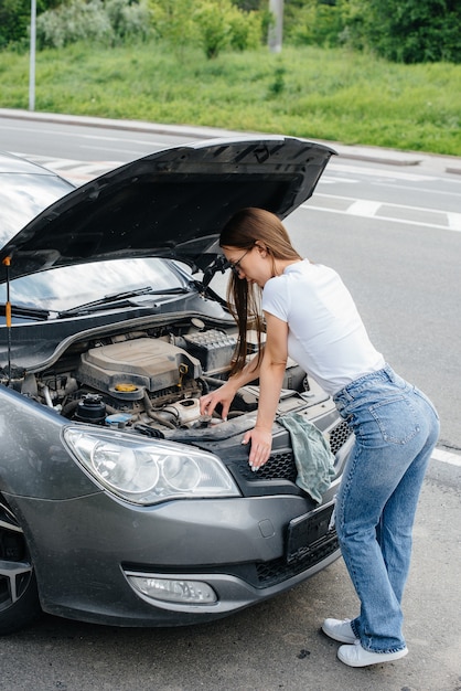 Una ragazza sta vicino a un'auto in panne nel mezzo dell'autostrada e guarda sotto il cofano. Guasto e guasto dell'auto. In attesa di aiuto.