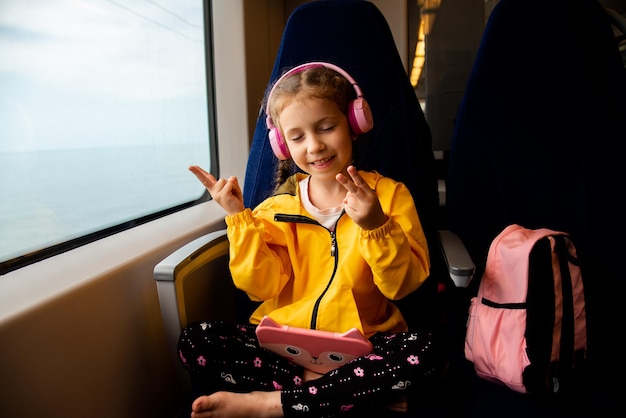 Una ragazza su un treno ascolta musica in cuffia con un gadget in mano Estate