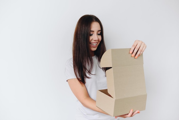 Una ragazza su uno sfondo bianco con i capelli fluenti apre una piccola scatola con un'espressione gioiosa sul viso
