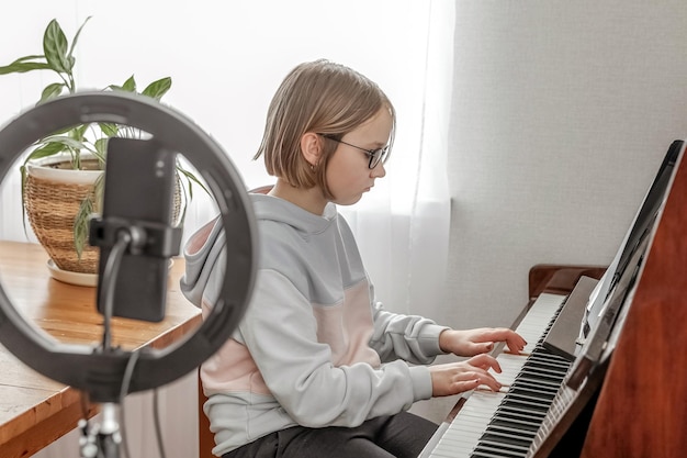 Una ragazza suona il piano con una lampada ad anello per una formazione a distanza su smartphone