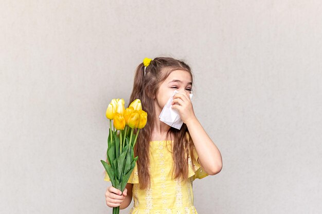 Una ragazza tiene in mano un bouquet di fiori primaverili e si copre il naso per evitare i sintomi dell'allergia