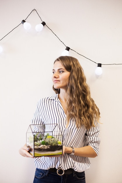 Una ragazza tiene in mano un florariumov, a forma di vetro con piante grasse, pietre e sabbia, decorato con nastri natalizi. Regali di Natale per casa e ufficio