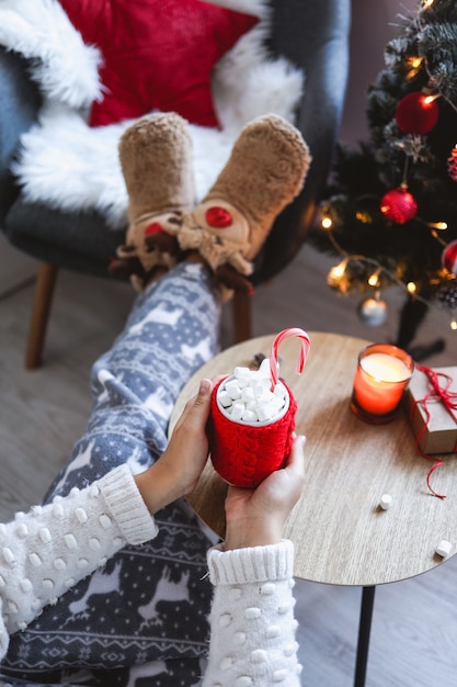 Una ragazza tiene in mano una tazza di cacao con marshmallow e caramelle. Atmosfera accogliente di Capodanno