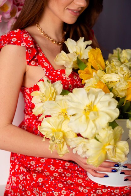Una ragazza tiene molti tulipani nelle sue mani il giorno della donna Capelli lunghi del bel vestito rosso