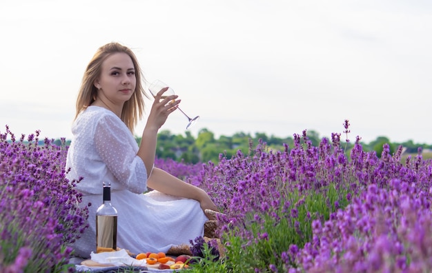 Una ragazza tiene un bicchiere di vino bianco sullo sfondo di un campo di lavanda Una ragazza beve vino in un campo di lavanda