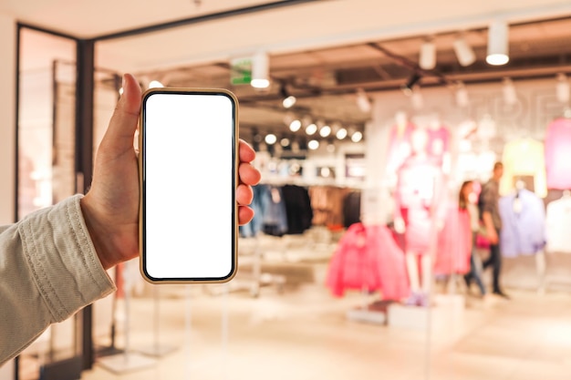 Una ragazza tiene un telefono in mano con uno schermo vuoto isolato sullo sfondo di un centro commerciale sfocato