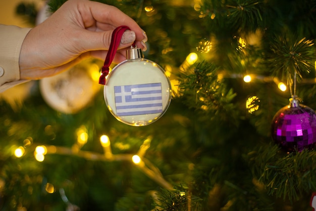 Una ragazza tiene una decorazione su un albero di natale con la bandiera della grecia