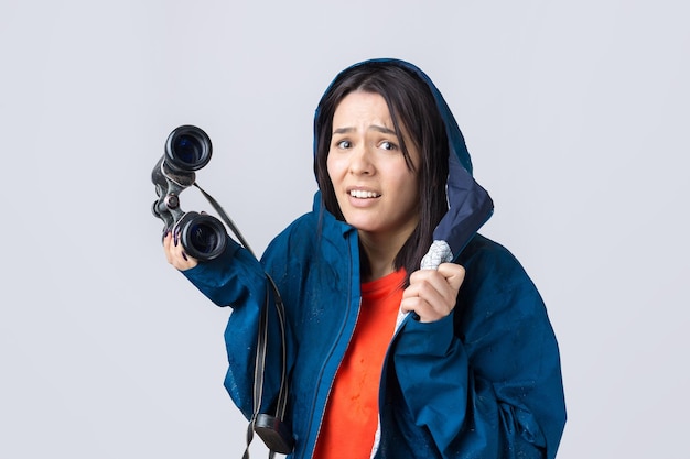 Una ragazza turistica con un impermeabile blu tiene in mano un binocolo e guarda lontano, spie.