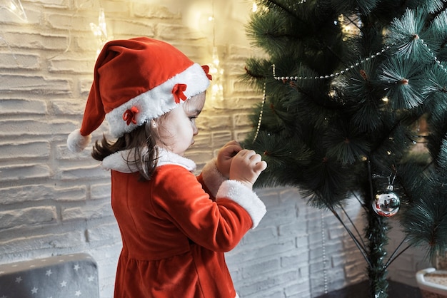 Una ragazza vestita da Babbo Natale sta decorando un albero di Natale