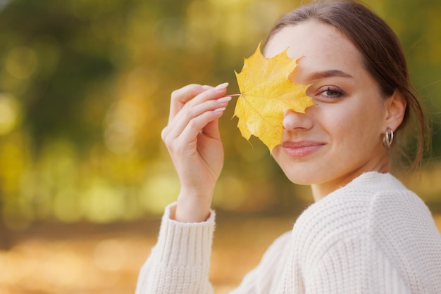 una ragazza vestita di giallo in un parco autunnale gioisce in autunno con le foglie gialle tra le mani