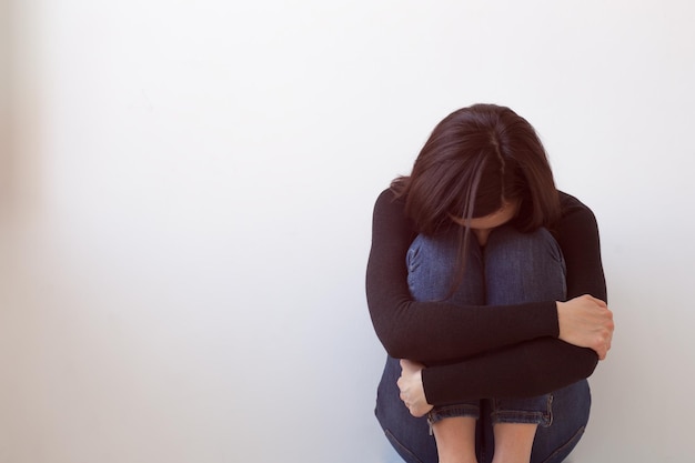 Una ragazza vestita di nero siede da sola vicino al muro bianco Soffre di solitudine e vergogna