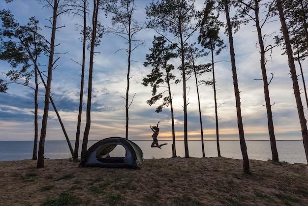 Una ragazza vicino a una tenda sullo sfondo dell'acqua e della foresta. La ragazza vicino alla tenda.