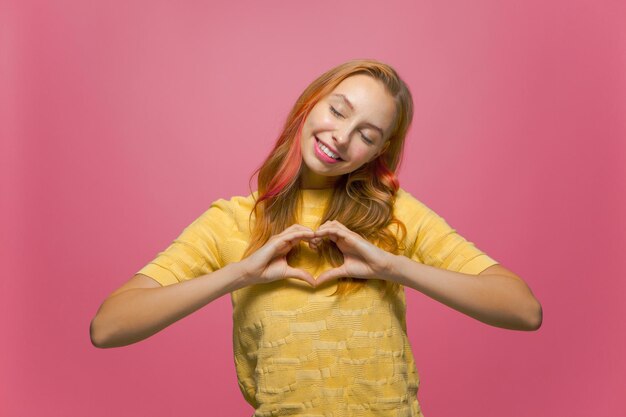 Una ragazza volontaria sorridente e amichevole fa il gesto del cuore con il segno dell'amore per il concetto di donazione di beneficenza del bene