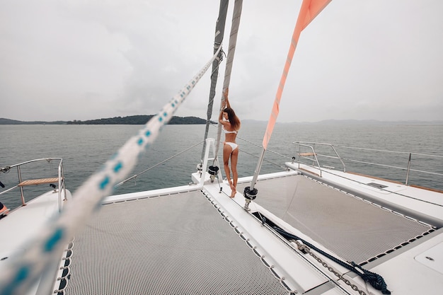 Una ragazza voltata indietro con un corpo fantastico in un costume da bagno aderente bianco è in piedi tra due reti in poliestere per yacht