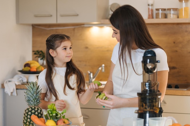 Una ragazzina adorabile che aiuta sua madre a fare il succo fresco a casa due femmine in grembiule frutta e