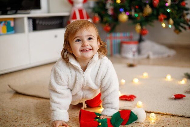 Una ragazzina adorabile che si diverte su un tappeto morbido davanti a un albero di Natale