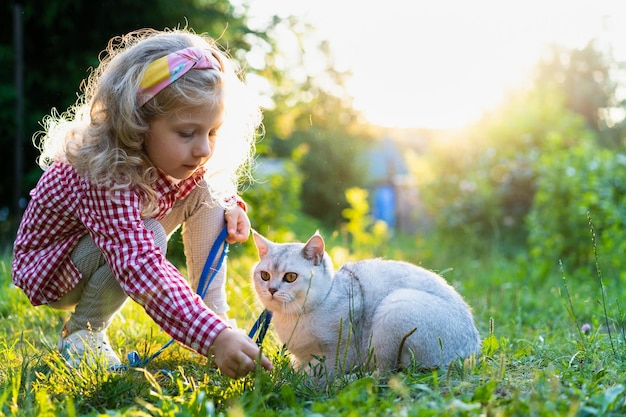 una ragazzina bionda che cammina con un gatto bianco di razza al guinzaglio.