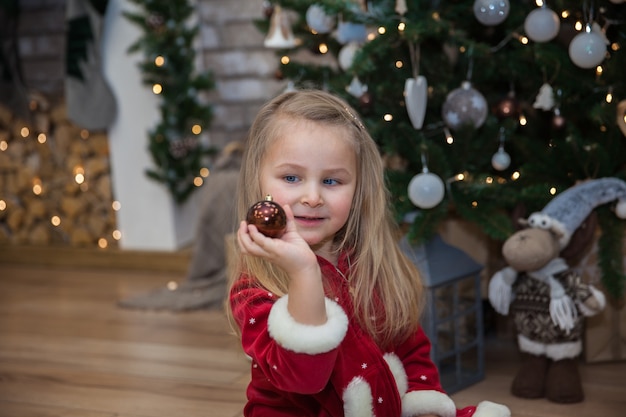 Una ragazzina carina con i regali di Natale seduta vicino all'albero di Natale nella stanza