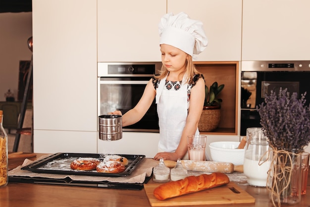 Una ragazzina carina con un cappello da chef bianco prepara i panini in cucina