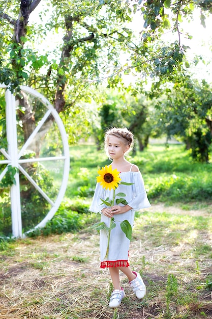 una ragazzina carina con un codino in testa tiene in braccio un bambino girasole con un girasole in giardino