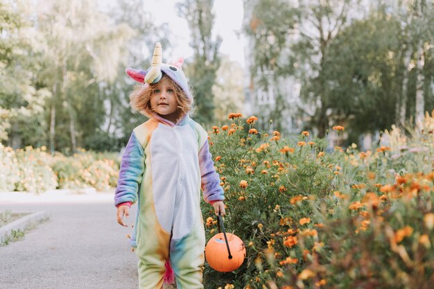 Una ragazzina carina con un costume da unicorno arcobaleno per Halloween va a raccogliere dolci nel cesto di zucca