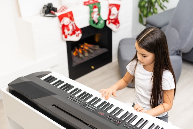 Una ragazzina carina suona la melodia di Natale al pianoforte, allegre feste di Natale, buone feste stagionali